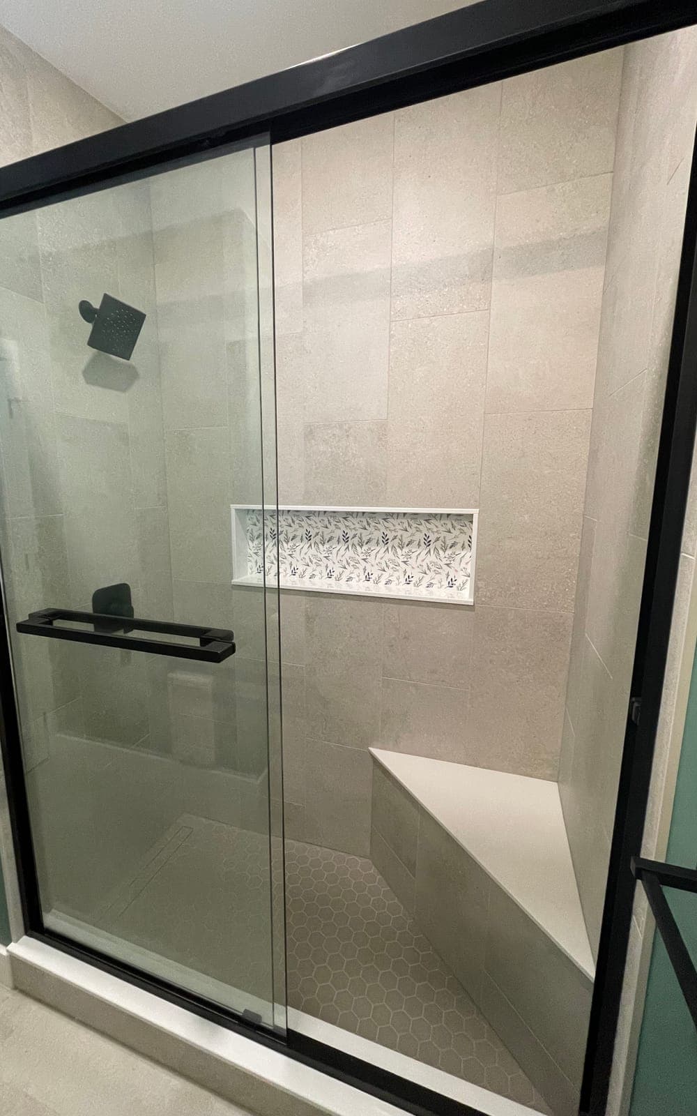 The new walk-in shower through black-framed sliding glass doors: a corner bench, the tiled niche and a hexagon tile floor