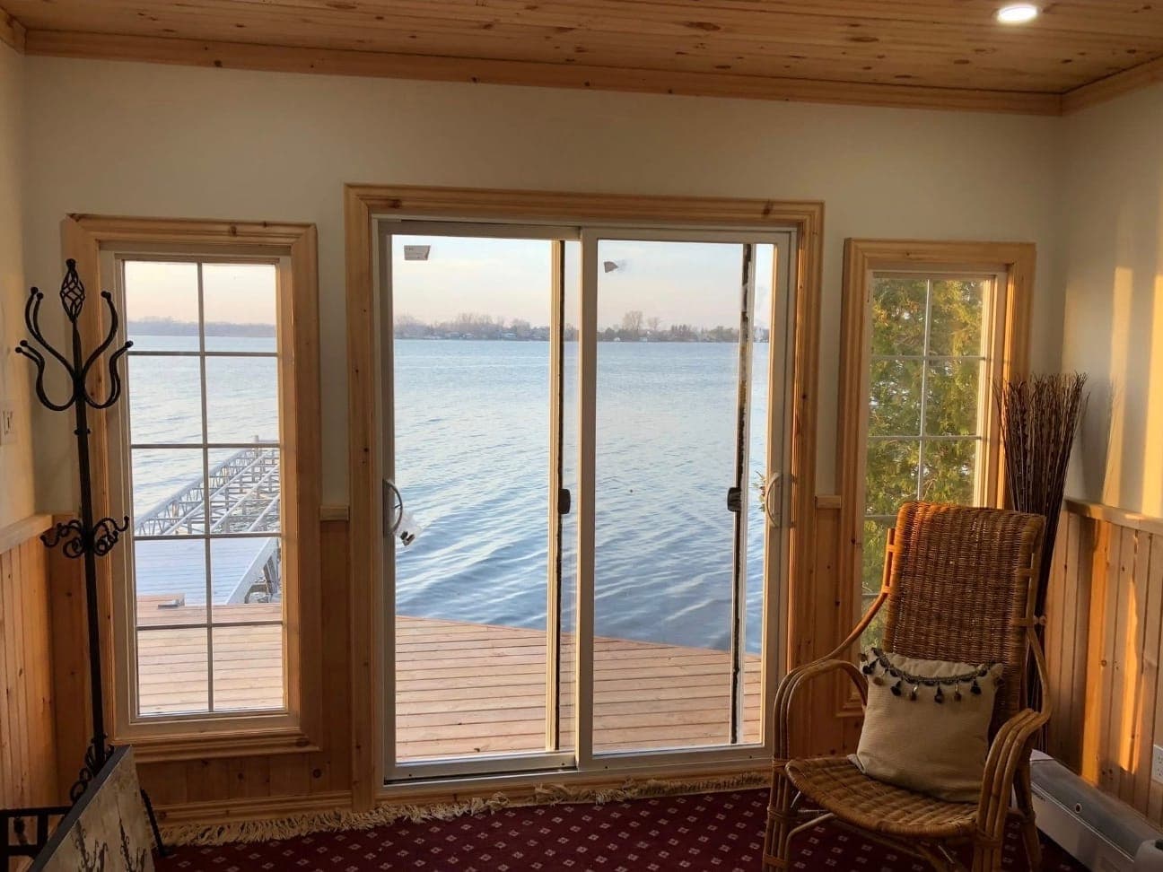 From inside the bunkie: pine-trimmed windows either side of a sliding patio door, looking out over the new deck to the lake