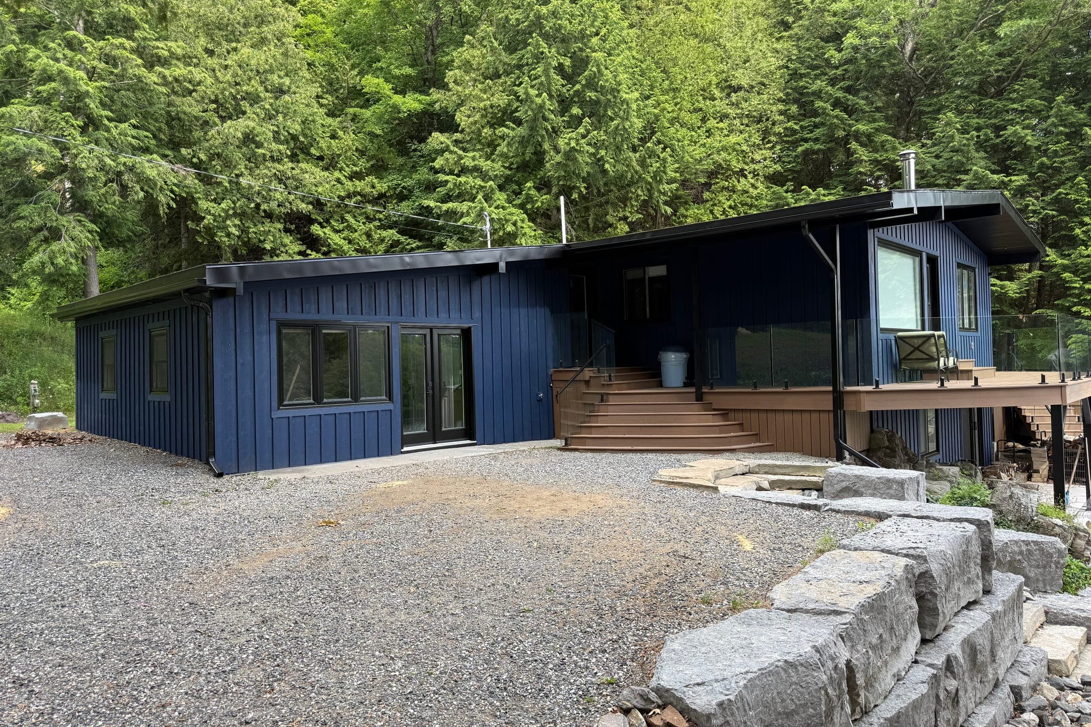 The whole cottage from the drive: dark blue board-and-batten siding, black windows and patio doors, and steps up to the deck