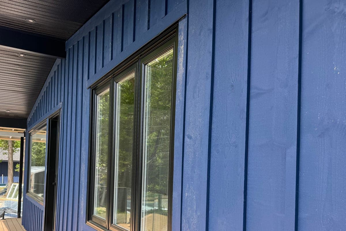 Along the wall: new black-framed windows in board-and-batten siding, under a black soffit with pot lights