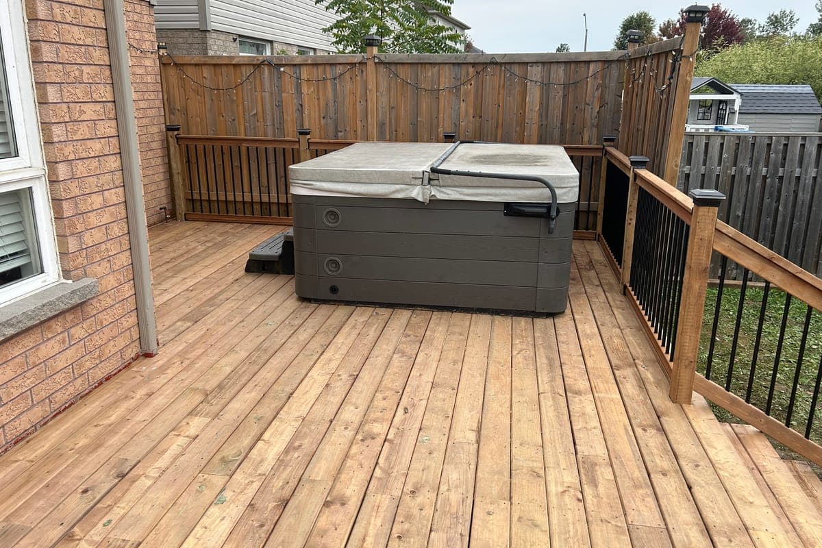 A hot tub sitting on the new deck, inside wooden railings with black pickets