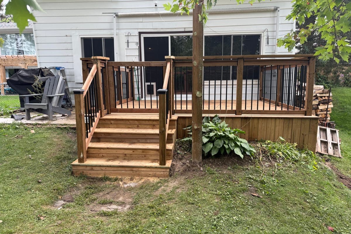 The finished deck from the lawn: new stairs, railings with black pickets, a gate at the top of the stairs and board skirting