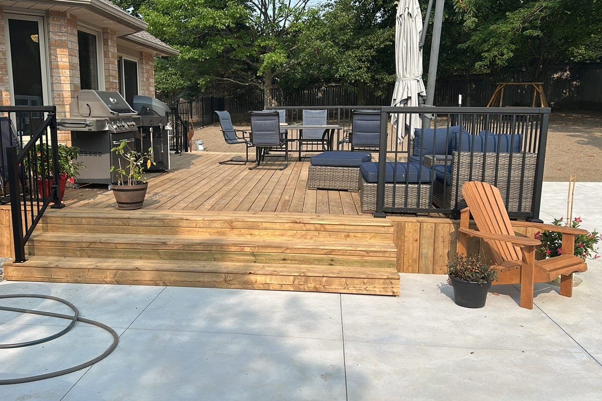 A poolside wood deck from the corner by the house, showing the wide stairs, black railings and board skirting