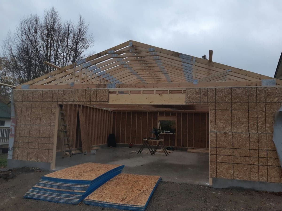 The same double garage part-way through: walls framed and sheathed on the slab, and the roof trusses up