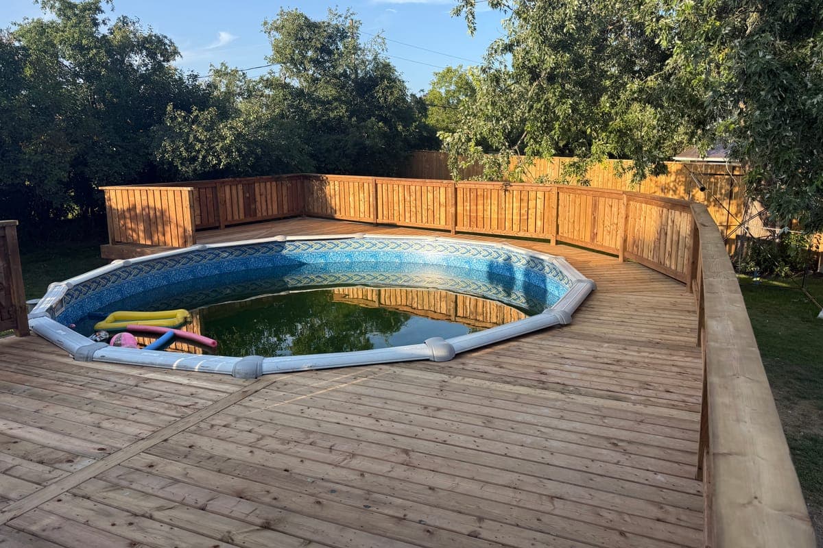 New wood decking right round an above-ground pool, with railings of upright deck boards